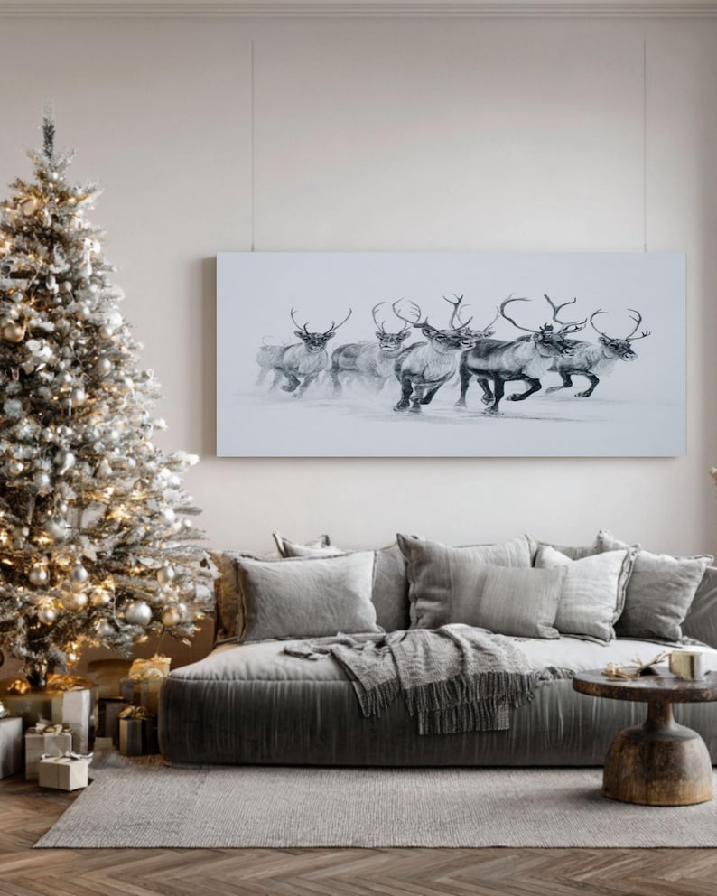 May include: A monochrome painting of reindeer running in snow is displayed above a grey sofa with cushions and a throw. A decorated Christmas tree stands to the left, with presents beneath it. The room has a neutral colour palette.