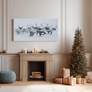 May include: A grayscale canvas print shows a herd of reindeer running across a snowy scene. The artwork hangs above a fireplace decorated for the festive season, with a Christmas tree and wrapped gifts. The reindeer are depicted in shades of grey and white.