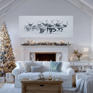 May include: A monochrome drawing of reindeer in motion, displayed above a white fireplace in a room decorated for Christmas. The scene includes a festive tree and a white sofa, creating a seasonal atmosphere.