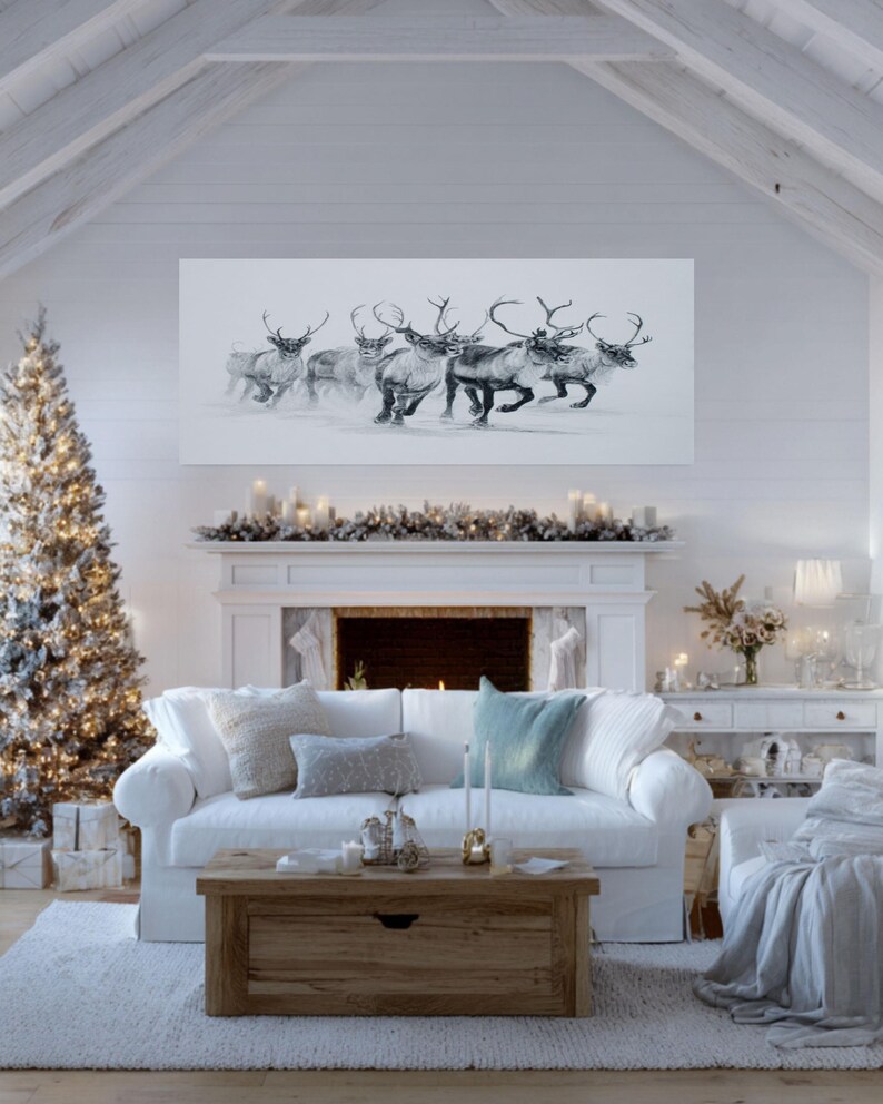 May include: A monochrome drawing of reindeer in motion, displayed above a white fireplace in a room decorated for Christmas. The scene includes a festive tree and a white sofa, creating a seasonal atmosphere.