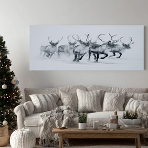 May include: A monochrome canvas print shows a group of reindeer running through snow. The rectangular artwork hangs above a beige sofa with cushions. A Christmas tree with lights and decorations is on the left.