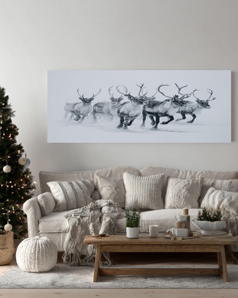 May include: A monochrome canvas print shows a group of reindeer running through snow. The rectangular artwork hangs above a beige sofa with cushions. A Christmas tree with lights and decorations is on the left.