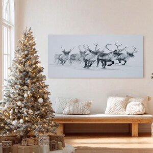 May include: A monochrome artwork shows reindeer running in snow. A decorated Christmas tree with lights and white baubles is on the left. A wooden bench with cushions is in front of the artwork, creating a festive scene.
