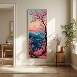 May include: A framed vertical art print depicting a Japanese landscape with a cherry blossom tree. The artwork shows a sunset over blue mountains, with pink blossoms and a black tree trunk. The sky transitions from pink to blue.