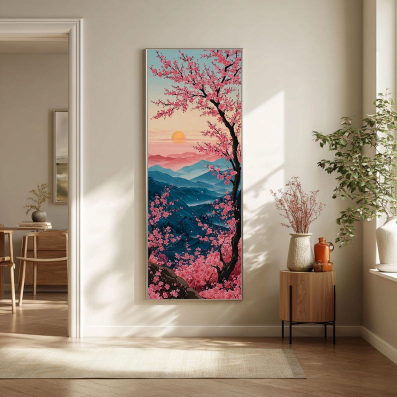 May include: A framed vertical art print depicting a Japanese landscape with a cherry blossom tree. The artwork shows a sunset over blue mountains, with pink blossoms and a black tree trunk. The sky transitions from pink to blue.