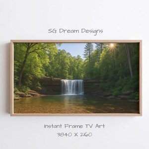 Puede incluir: Una impresión enmarcada de un paisaje de cascada que cae en una piscina clara, rodeada de exuberantes árboles verdes. El sol brilla a través de los árboles, creando una escena natural y brillante. El texto "SG Dream Designs" y "Instant Frame TV Art" son visibles.