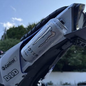 May include: A white Monster Energy Ultra can with black text and logo, featuring the words Zero Sugar, positioned on the rear section of a white motorcycle frame that displays Castrol and D.I.D brand decals against a clear blue sky background.