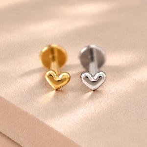 May include: Two stud earrings with heart-shaped tops. One earring is gold-toned with a polished finish, and the other is silver-toned with a polished finish. Each earring features a straight post extending from the back of the heart design.
