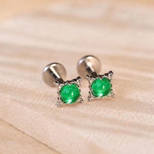 Peut inclure: Une paire de boucles d'oreilles à tige avec une pierre cabochon ronde d'un vert éclatant, sertie dans une monture en métal argenté à quatre griffes. Les boucles d'oreilles présentent un fermoir plat et circulaire à l'arrière.