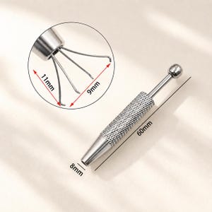 May include: A silver-colored parts grabber tool with a textured handle and a claw-like end. The tool is 60mm long, with the claw measuring 11mm by 9mm. The tip is 8mm wide. The tool has a ball-shaped end.