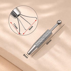 May include: A silver-toned metal prong holder tool with a knurled grip and a ball-end plunger. The tool measures 60mm in length and 8mm in diameter. An inset shows the four-prong claw extended, measuring 11mm by 9mm for precise small object handling.