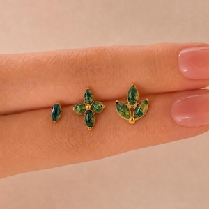 May include: Three gold stud earrings featuring marquise-cut green moss agate stones. The set includes a single marquise stone, a four-stone flower-shaped cluster, and a three-stone fan-shaped arrangement, all set in polished gold metal settings.