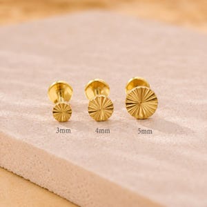 May include: Three gold-toned flat back stud earrings with a sunburst texture on the circular face. The earrings are arranged in a row with labels indicating sizes of 3mm, 4mm, and 5mm, showing the varying diameters of the textured circular heads.