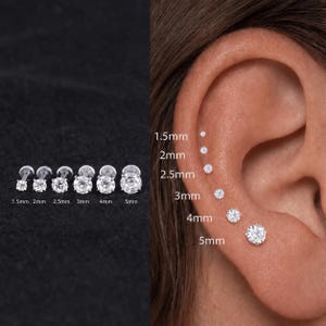 May include: A set of six silver-toned stud earrings with clear round stones, ranging in size from 1.5mm to 5mm. The earrings are displayed individually and shown worn in a row on an ear, with labels indicating the specific size of each stud.