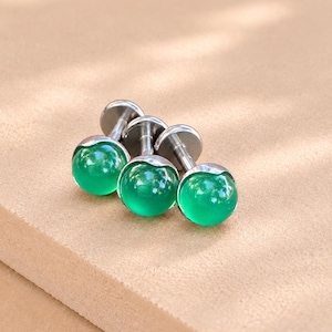May include: Three stud earrings featuring smooth, round, vibrant green cabochon stones set in polished silver-tone metal posts. Each earring has a flat circular back and a short stem, showcasing a minimalist design with a glossy, reflective finish.