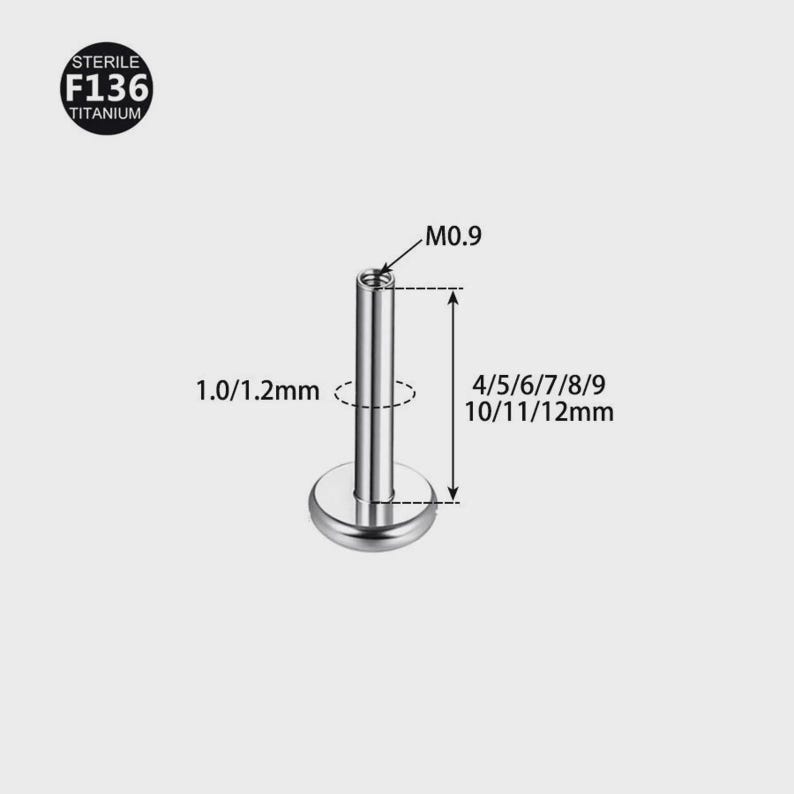 Op de afbeelding: Een zilverkleurige titanium labret-stud met een platte ronde basis en een schroefdraadstaafje. De afbeelding toont technische specificaties: M0.9 schroefdraad, 1.0/1.2mm dikte en lengtes van 4mm tot 12mm. Een badge vermeldt Sterile F136 Titanium.