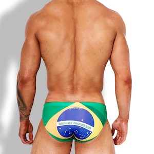 May include: Swim briefs featuring the green, yellow, and blue colours of the Brazilian flag. The design includes a central blue circle with a white horizontal band containing the text "ORDEM E PROGRESSO" and small white stars throughout.