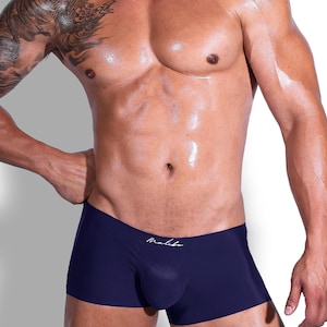 May include: A pair of solid navy blue boxer briefs featuring a low-rise waistband and a contoured front pouch. The garment displays the word Malibu in a white cursive script font centred just below the waistband on the front panel.