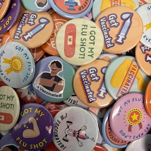 Könnte beinhalten: Eine Sammlung bunter runder Buttons mit verschiedenen Designs und Texten zum Thema Impfen. Die Buttons zeigen Bilder von Spritzen, Pflastern und Sätzen wie "Get Vaccinated" und "I Got My Flu Shot!"