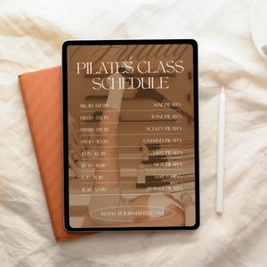 Puede incluir: Una tableta digital muestra un horario de clases de Pilates con horarios y tipos de clases. La tableta está junto a un cuaderno naranja y un lápiz óptico blanco. El horario incluye clases como Mat Pilates y Hot Pilates. La web es visible.