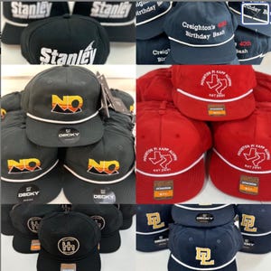 May include: Assortment of black, red, and navy blue baseball caps. Some caps feature the text "Stanley" in white, while others display logos and text such as "NO", "Creighton's 40th Birthday Bash", and "Houston Pi Kapp Alumni".