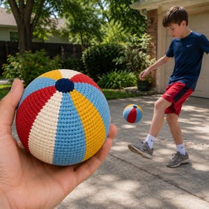 May include: A colorful, crocheted ball with red, white, blue, and yellow panels, held in a hand. A second ball is kicked by a person in a blue shirt and red shorts. The ball is approximately 6 inches in diameter.