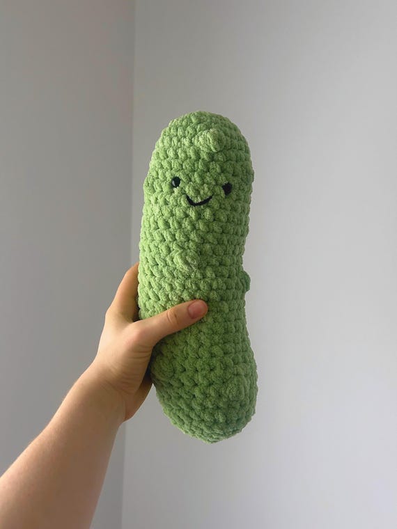 A giant hand-crocheted dill pickle plush — chunky, absurd, and unmistakably made by a human with a sense of humor.