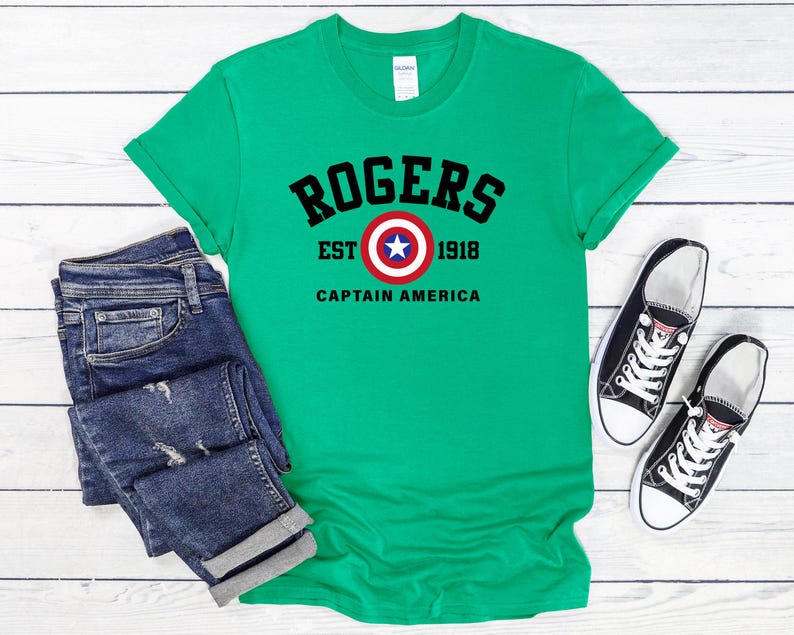 May include: A green t-shirt with the text "ROGERS EST 1918 CAPTAIN AMERICA" in black. The shirt features a Captain America shield graphic. Dark blue jeans and black and white sneakers are also in the image.