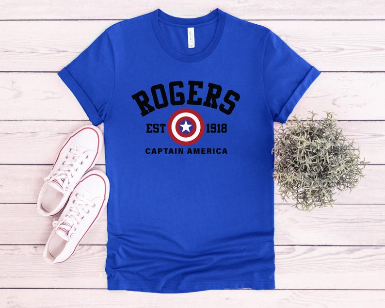 May include: Royal blue t-shirt with the text "ROGERS EST 1918 CAPTAIN AMERICA" in black and white. The design includes a circular emblem with a white star on a red and white background. White canvas sneakers are on the left.