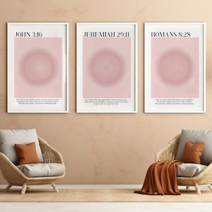 Puede incluir: Tres impresiones artísticas enmarcadas con bordes blancos. Cada impresión presenta un diseño circular rosa y blanco y texto de la Biblia: Juan 3:16, Jeremías 29:11 y Romanos 8:28. Las impresiones se muestran sobre dos sillas de mimbre.