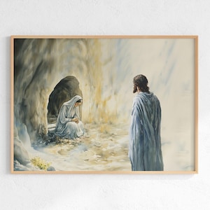 May include: Watercolor print of a religious scene. A figure in a white robe sits near a cave entrance, while another figure in a blue robe stands nearby. The artwork is framed in a light brown wooden frame.