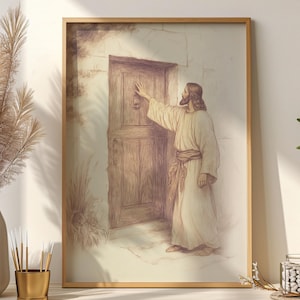 May include: A framed sepia-toned print depicts a figure in a robe knocking on a wooden door. The artwork has a vintage aesthetic, with soft shading and a warm color palette. The frame is a light wood color.