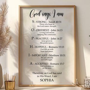 May include: A framed print featuring the words "God says I am" in a decorative script. The print lists positive affirmations, including "Strong," "Obedient," and "Hopeful," with associated Bible verses. The name "Sophia" is at the bottom.