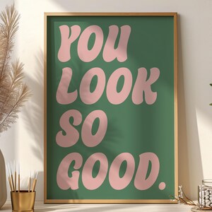 以下が含まれることがあります： 緑色の背景にピンク色の丸みを帯びた文字で「YOU LOOK SO GOOD」と書かれた額入りのアートプリント。 フレームは薄茶色です。 インテリアデコレーションに適しています。