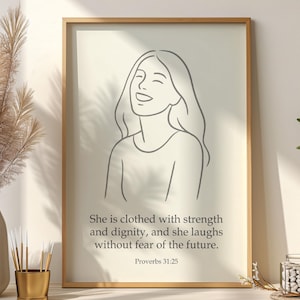 May include: A framed print featuring a line drawing of a smiling person. The artwork is in a neutral color palette, with the text "She is clothed with strength and dignity, and she laughs without fear of the future. Proverbs 31:25."
