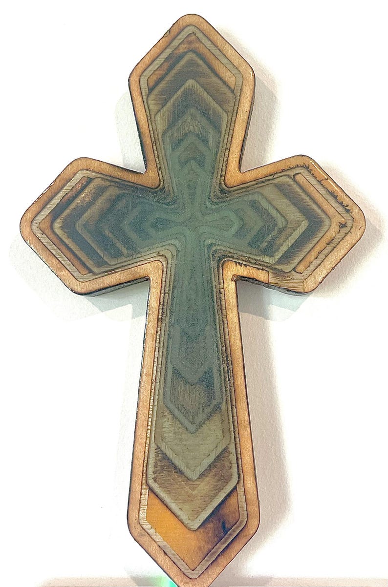 May include: Wooden cross with a layered design. The cross features a natural wood border and a central design with shades of green, brown, and yellow. The layered effect creates depth and dimension, suitable for religious decor.