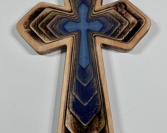 May include: Wooden cross with a layered design. The cross features a light brown outer layer, with a blue and brown gradient in the center. The cross is a religious symbol.