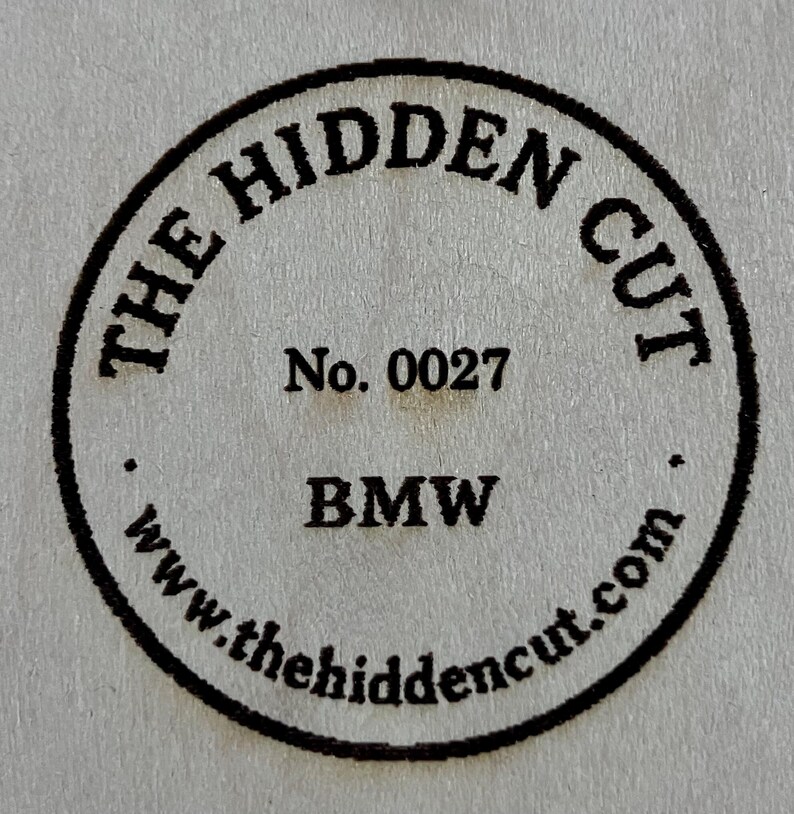 May include: A circular black stamp with the text "THE HIDDEN CUT" around the top and "www.thehiddencut.com" around the bottom. The stamp also includes "No. 0027" and "BMW" in the center.