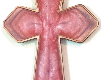 May include: A decorative cross with a wooden frame and a pink resin center. The cross has a layered design with a lighter pink hue in the center and a darker pink outline. The wooden frame adds a natural contrast.