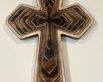 May include: A layered wooden cross with a detailed design. The cross features a series of nested shapes, creating a three-dimensional effect. The wood has a natural, warm tone with darker accents, and the edges are smooth.