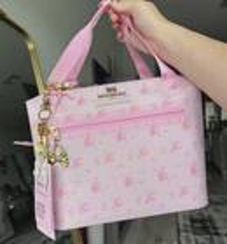 Peut inclure: Un sac &agrave; main rose clair avec un motif r&eacute;p&eacute;titif de petites ic&ocirc;nes rose fonc&eacute;. Le sac poss&egrave;de deux anses, une poche frontale zipp&eacute;e horizontale et une breloque en m&eacute;tal dor&eacute; attach&eacute;e sur le c&ocirc;t&eacute;. Le texte "MINISO" est imprim&eacute; sur le devant.
