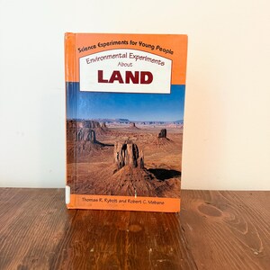 May include: A hardcover book titled "Science Experiments for Young People" with the subtitle "Environmental Experiments About LAND." The cover features a desert landscape with mesas under a blue sky. The book is orange and blue.