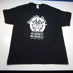 May include: Black t-shirt with a white graphic featuring the text "Double Dees" above an illustration of two figures. Below the graphic is the text "921 Decatur St. New Orleans LA".