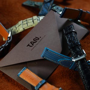 May include: A white ceramic mug with a black handle and the text "But First, Coffee" in a bold, black font. The mug is set against a blurred background, suggesting a cozy setting.