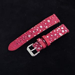 May include: A two-piece watch strap in a vibrant magenta pink color with a textured, bumpy surface featuring metallic silver accents. The strap includes a polished silver-tone metal buckle and two matching magenta leather keepers for securing the band.