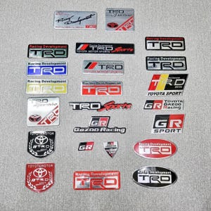May include: A collection of TRD and GR sport emblem badges in various shapes and sizes. The badges feature the text "Racing Development", "Toyota Motor Sports", and "Gazoo Racing" in red, black, silver, and blue.