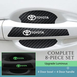 May include: An 8-piece set of black carbon fiber textured car door handle protectors featuring the white Toyota logo and text. The set includes 4 door bowl inserts and 4 door handle covers, with a luminous upgrade that glows in the dark.