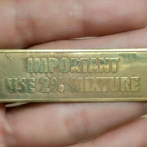 Peut inclure: Plaque métallique rectangulaire de couleur laiton avec le texte en relief "IMPORTANT USE 2% MIXTURE". La plaque a des coins arrondis et semble légèrement usée. Le texte est centré.