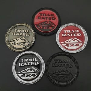 May include: Five circular Trail Rated 4x4 emblems in various colors. The emblems feature a mountain range graphic and the text "TRAIL RATED" and "4x4". Colors include red, black, silver, and bronze.