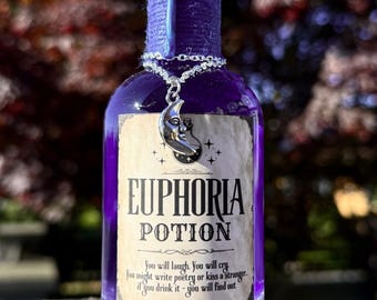 Könnte beinhalten: Eine lila Flaschen mit einem silbernen Mond-Anhänger. Die Flasche hat ein Etikett mit der Aufschrift "Euphoria Potion" und Text darunter. Die Flasche ist mit lila Wachs versiegelt.